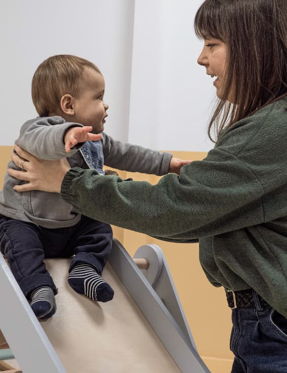 Un bébé accompagné de sa maman fait du toboggan à La Cité des Petits Rêveurs