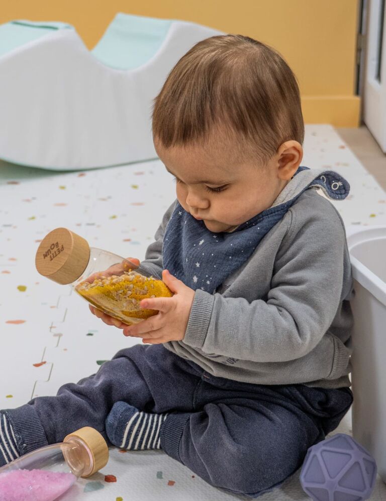 un bébé découvre les sons avec une bouteille pleine de grains à la Cité des Petits Rêveurs